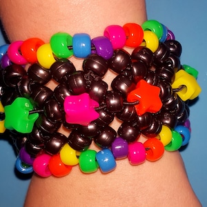 May include: A vibrant beaded bracelet with a mix of black, rainbow, and star-shaped beads. The bracelet is made of small, round black beads with accents of bright colours like pink, orange, yellow, green, and blue. Star-shaped beads add a playful touch.