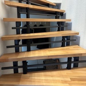 Könnte beinhalten: Eine Holztreppe mit hellfarbenen Stufen und schwarzen Metallstützen. Die Stufen sind hellbraun und haben eine glatte Oberfläche. Die Treppe hat ein modernes Design und befindet sich in einem Innenraum.