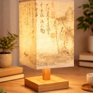 May include: A rectangular table lamp with a wooden base and a shade featuring a traditional Asian landscape painting. The lamp has a square wooden base, a rectangular shade, and a warm, inviting glow.