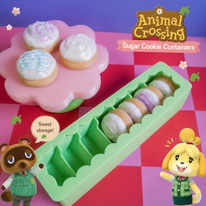 Pode incluir: Um recipiente verde claro cheio de biscoitos de a&ccedil;&uacute;car, ao lado de uma bandeja rosa em forma de flor com biscoitos. Os biscoitos t&ecirc;m cobertura branca e granulado colorido. A imagem tem o texto "Animal Crossing Sugar Cookie Containers."