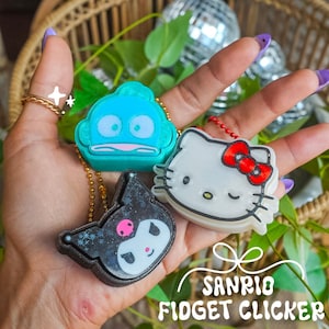 May include: Three Sanrio character fidget clickers on gold and red ball chains. One is a teal Hangyodon, one is a white Hello Kitty with a red bow, and one is a black Kuromi with a pink skull detail. The text SANRIO FIDGET CLICKER is visible.