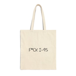 May include: Cream-colored tote bag with black text that reads "F*CK I-QS". The bag has a rectangular shape with a handle made of the same material. The text is centered on the front of the bag.