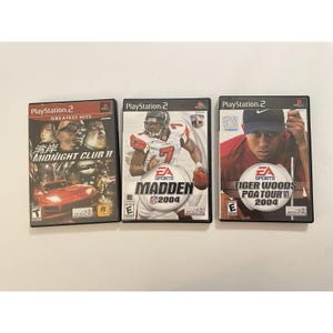 May include: Three PlayStation 2 video game cases featuring Midnight Club II, Madden 2004, and Tiger Woods PGA Tour 2004. Each case displays its respective game title, cover art, and the ESRB rating symbol on the front of the plastic game box.