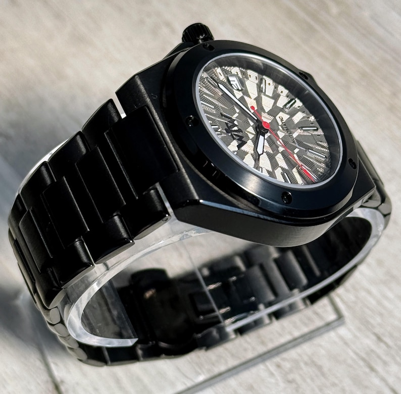 K&ouml;nnte beinhalten: Eine mattschwarze automatische Armbanduhr mit einem strukturierten grauen und schwarzen geometrischen Zifferblattmuster. Die Uhr verf&uuml;gt &uuml;ber ein schwarzes Metallgliederarmband, einen roten Sekundenzeiger, wei&szlig;e Stunden- und Minutenzeiger sowie ein Datumsfenster.