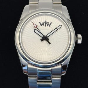 Puede incluir: Un reloj de pulsera de acero inoxidable en tono plateado con una esfera blanca de patr&oacute;n radial y el texto WTW impreso en negro. El reloj incluye una correa de metal de tres eslabones, una corona en el lado derecho y manecillas con bordes negros.