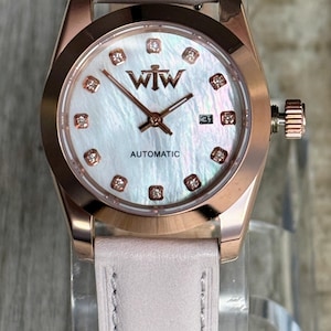 May include: A rose gold-tone wristwatch with a mother-of-pearl dial, featuring the text WTW and AUTOMATIC. The dial includes small crystal hour markers and a date window at the three o'clock position. It has a light pink leather strap.