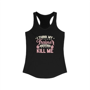 May include: Black racerback tank top with the text "I THINK MY TRAINER IS TRYING TO KILL ME" in pink and white. The design includes a barbell graphic. A humorous fitness-themed apparel item.