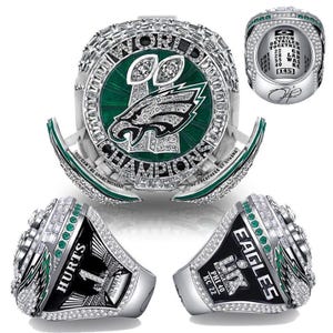 Peut inclure: Une bague de championnat argentée avec un design vert et blanc. La bague présente les mots "WORLD CHAMPIONS" et le logo des Eagles de Philadelphie. La bague porte également les inscriptions "HURTS 1" et "EAGLES SUPER BOWL PHI 40 KC 22".