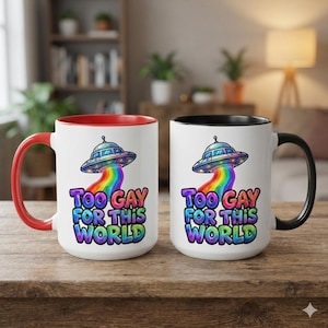 May include: Two white ceramic mugs featuring a colourful graphic of a UFO beaming down a rainbow. The text "TOO GAY FOR THIS WORLD" is printed in a vibrant, multi-coloured bubble font. One mug has a red handle and rim, while the other has a black handle and rim.