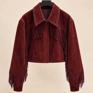 May include: A deep burgundy suede jacket featuring a pointed collar, a front button closure, and long sleeves. The garment is detailed with long, flowing fringe trim that extends across the chest and down the length of each sleeve.