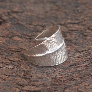 May include: A silver ring with a textured, leaf-shaped design. The ring is open and adjustable.