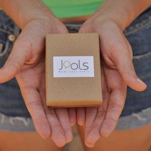 May include: A person is holding a brown box with the words "Jools Wear your story" printed on it.