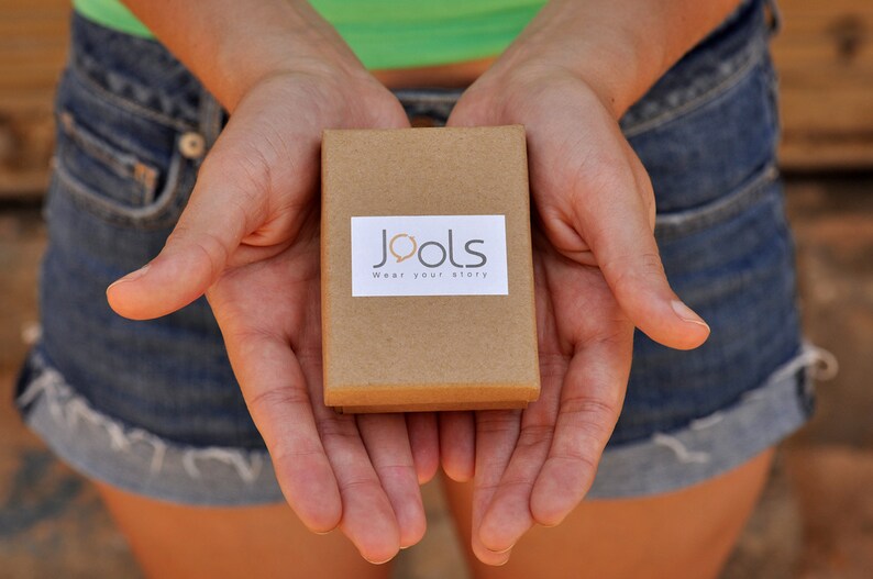 Op de afbeelding: Een persoon houdt een bruine doos vast met de tekst "Jools Wear your story" erop.