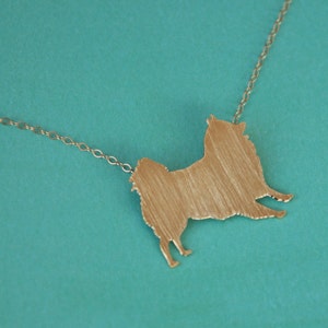 Op de afbeelding: Een gouden ketting met een hanger in de vorm van een hondensilhouet. De hanger is een eenvoudige schets van een hond, zonder details.