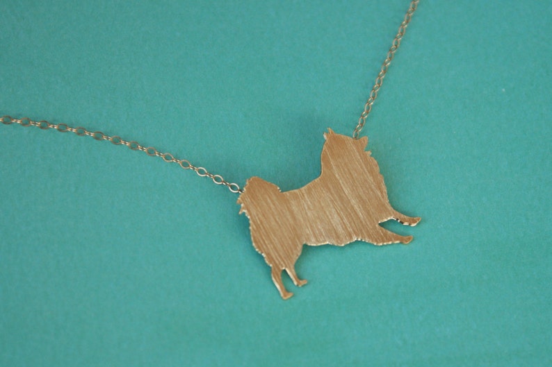 Op de afbeelding: Een gouden ketting met een hanger in de vorm van een hondensilhouet. De hanger is een eenvoudige schets van een hond, zonder details.