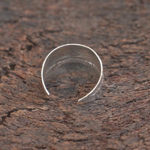 May include: A silver ring with a hammered texture. The ring is open and has a slightly curved shape.