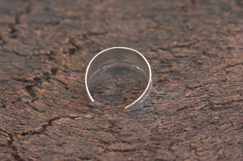 May include: A silver ring with a hammered texture. The ring is open and has a slightly curved shape.