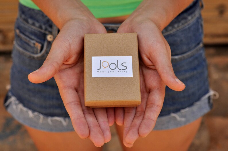 May include: A person is holding a small brown box with the words "Jools Wear your story" printed on it.