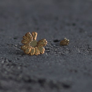 Puede incluir: Un par de pendientes de oro en forma de flor. Los pendientes son pequeños y delicados, y serían un gran regalo para un amigo o un ser querido.