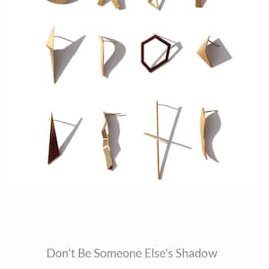 May include: A collection of gold and brown geometric earrings, including a circle, an X, a triangle, a rectangle, a curved shape, a hexagon, a triangle, a curved shape, a triangle, a wavy shape, a cross, and a curved shape. The text "Don't Be Someone Else's Shadow" and "WEAR YOUR OWN STORY." is displayed below the earrings. The word "Jools" is displayed below the text in a stylized font with a speech bubble.