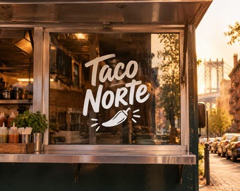 May include: A dark green food truck features a large white decal on its window that reads Taco Norte above a graphic of a chili pepper. The interior shows stainless steel surfaces and containers, while the exterior reflects a city street.