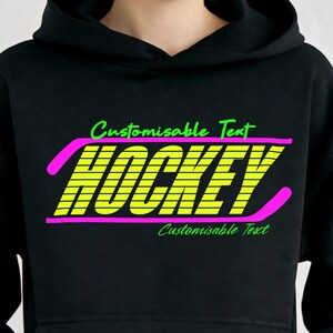 May include: Black hoodie featuring the word "HOCKEY" in neon yellow, outlined in pink, with the text "Customisable Text" above and below. The hoodie is worn by a person with light skin and blue eyes.