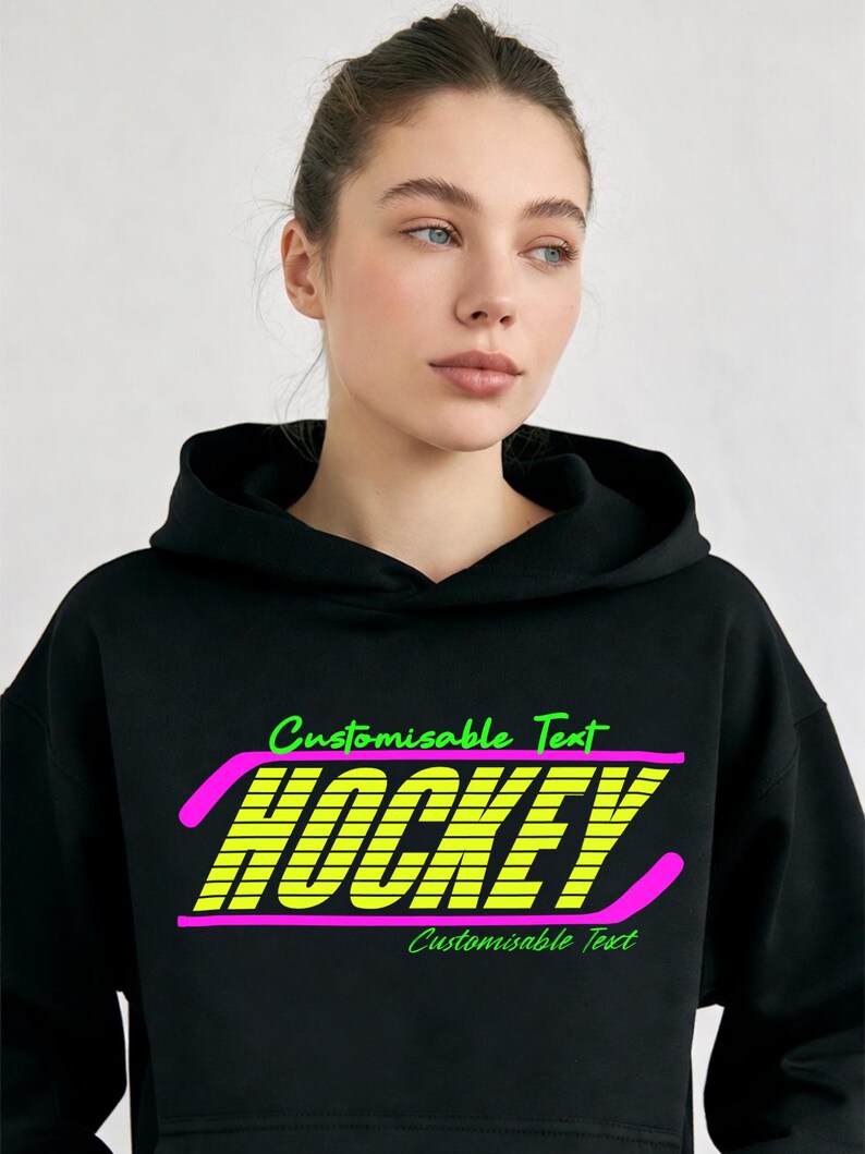 May include: Black hoodie featuring the word "HOCKEY" in neon yellow, outlined in pink, with the text "Customisable Text" above and below. The hoodie is worn by a person with light skin and blue eyes.