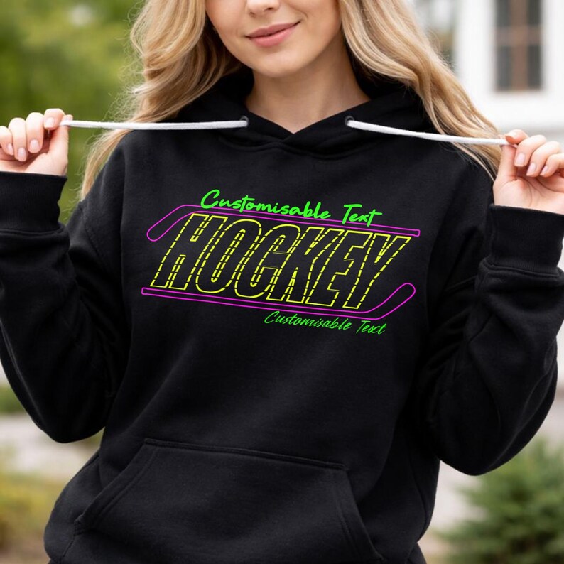 May include: Black hoodie with a neon green and purple hockey design. The word "HOCKEY" is in a yellow, dashed font, outlined in purple. Above and below the word are the words "Customisable Text" in green. The hoodie has a drawstring hood and a front pocket.
