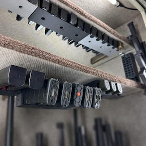 May include: Interior view of a gun safe, showcasing multiple black magazine holders mounted on the ceiling and a shelf. The holders are filled with magazines. The safe's interior is lined with a tan fabric.