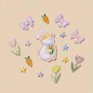 May include: Embroidered patches featuring a white bunny wearing a hat and holding flowers, surrounded by carrots, bows, stars, and tulips. The patches are in pastel colors, perfect for Easter or spring-themed crafts.