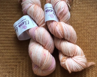 May include: Two skeins of yarn in a peach and white colourway. The yarn is hand-dyed and has a variegated colour pattern. The yarn is labelled "Clean Colors" and "Hand-dyed in Maine".
