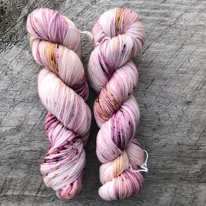 Pode incluir: Dois novelos de fio em uma combina&ccedil;&atilde;o de cores rosa, branco e dourado com manchas de cor em toda a superf&iacute;cie. O fio est&aacute; enrolado em forma de bola.