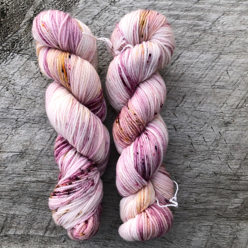 Pode incluir: Dois novelos de fio em uma combina&ccedil;&atilde;o de cores rosa, branco e dourado com manchas de cor em toda a superf&iacute;cie. O fio est&aacute; enrolado em forma de bola.
