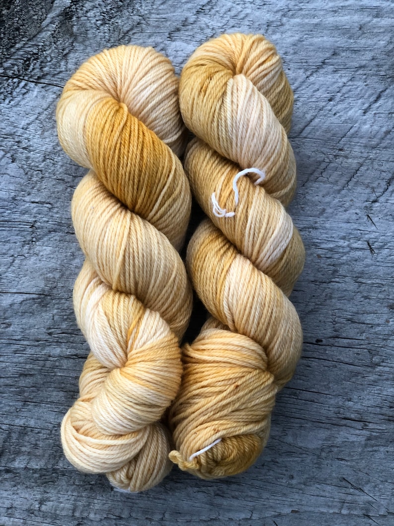Pode incluir: Dois novelos de fio em um degrad&ecirc; de creme e amarelo. O fio &eacute; tingido &agrave; m&atilde;o e tem uma textura macia e felpuda.
