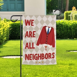May include: A garden flag displaying the text "WE ARE ALL NEIGHBORS" in red. The flag design includes a red cardigan, white shirt, and blue tie illustration. The background has a diamond pattern.