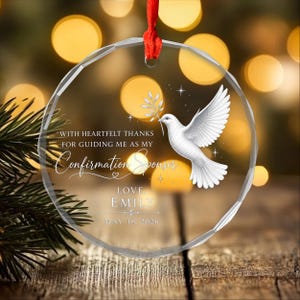 May include: A circular clear glass ornament with a red ribbon hanger featuring a white dove illustration holding an olive branch. Text reads: WITH HEARTFELT THANKS FOR GUIDING ME AS MY Confirmation Sponsor LOVE, EMILY MAY 18, 2026.