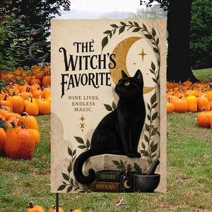 Peut inclure: Un drapeau de jardin rectangulaire avec un chat noir assis sur un bloc de pierre. Le texte indique THE WITCH'S FAVORITE NINE LIVES. ENDLESS MAGIC. HERBS POTIONS. Comprend un croissant de lune, des vignes, une fiole et un mortier.