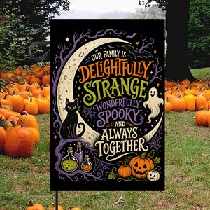 Peut inclure: Un drapeau de jardin rectangulaire sur fond noir orné d'un grand croissant de lune, d'un chat noir, d'un fantôme blanc, de trois flacons de potion en verre et de deux citrouilles. Le texte indique : Our family is delightfully strange, wonderfully spooky and always together.