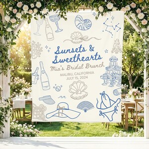 May include: A white fabric banner featuring blue and tan line art illustrations of seashells, champagne, a bikini, a sun hat, and a campfire. The text reads Sunsets & Sweethearts, Mia's Bridal Brunch, MALIBU, CALIFORNIA, JULY 15, 2024.
