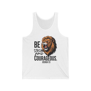 May include: White tank top with a roaring lion graphic in shades of brown and orange. The text "BE STRONG AND COURAGEOUS. JOSHUA 1:9" is printed in black. A casual, sleeveless shirt.
