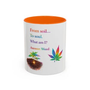 May include: White ceramic mug with an orange interior. The mug features the text "From soil... To soul. What am I? Answer: Weed." with illustrations of a cannabis plant and leaf in rainbow colors.
