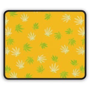 May include: A rectangular mousepad with a yellow background and a repeating pattern of green and white cannabis leaves. The mousepad has a black border.