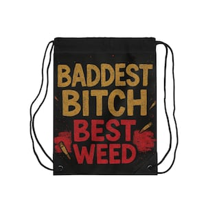 Op de afbeelding: Zwarte trekkoordtas met de woorden "BADDEST BITCH BEST WEED" in gouden en rode letters. De tas heeft een zwarte achtergrond met een rood spatterontwerp en kogelillustraties.