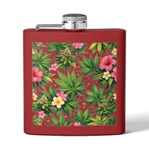 Puede incluir: Un petaca rojo de acero inoxidable con tapa y bisagra plateadas. La petaca presenta un vibrante estampado de hojas verdes de cannabis, flores de hibisco rosas y flores de plumeria amarillas sobre un fondo rojo.