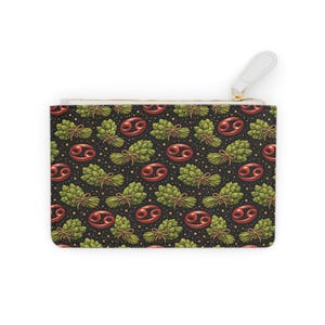 Puede incluir: Una bolsa negra con cremallera con un patrón repetido de lúpulo verde, símbolos del zodiaco Cáncer rojos y explosiones de estrellas doradas. La bolsa tiene una correa de muñeca blanca y una cremallera dorada.