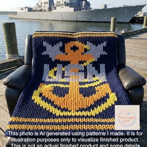 May include: A chunky knit blanket featuring a large gold anchor design centered on a dark navy blue background with light gray accents. The blanket displays horizontal gold stripes at the bottom edge and is draped over a black leather armchair.