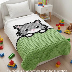 Puede incluir: Una manta tejida blanca y verde con un diseño de gato pixelado sobre una cama infantil. El gato es gris, negro y rosa. La cama está rodeada de bloques de construcción y juguetes coloridos. El texto en la parte inferior dice: "Esta foto es generada por IA y es solo para fines ilustrativos para visualizar el producto terminado. Este no es un producto terminado real."