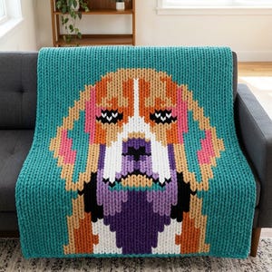 May include: A chunky knit throw blanket featuring a large, colorful pixelated portrait of a beagle dog. The blanket has a teal background with the dog rendered in shades of orange, tan, white, black, and purple using thick, textured yarn stitches.