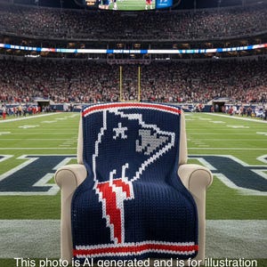 May include: A navy blue knitted blanket with a team logo in white and red, displayed on a beige armchair. The background shows a stadium filled with spectators. The text at the bottom says, "This photo is AI generated and is for illustration purposes only to visualize finished product."