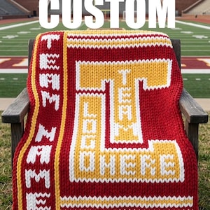 May include: A custom red, yellow, and white knitted blanket draped over a wooden chair. The blanket features a large letter "T" with the words "I AM HOME" and "TEAM" in white. The word "CUSTOM" is displayed across the top.
